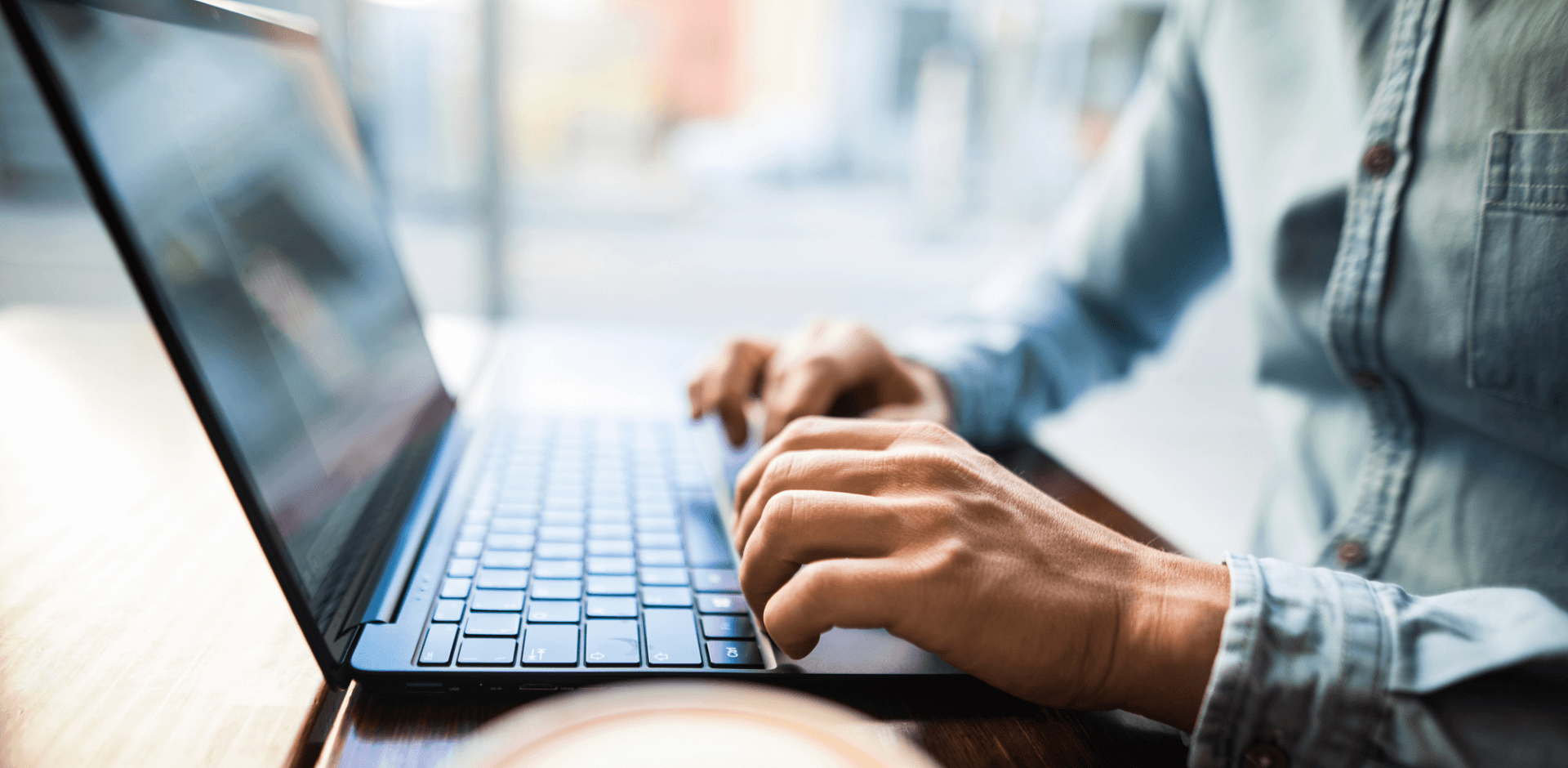 A young man typing on laptop, in an office or café, coffee cup in the bleed, close-up